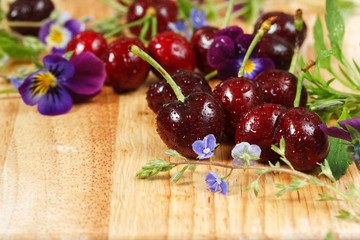 Cherries on wooden table with water drops macro background. With wildflowers. Closeup. 