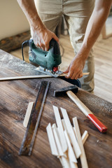 Men's hands with electric jig saws in the hand in the process of sawing wooden pieces. The concept of handmade.