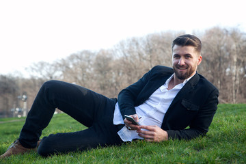 Geschäftsmann mit Smartphone ruht sich liegend auf einer Wiese im Park aus © Cara-Foto