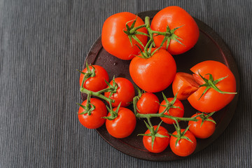 Fresh red ripe organik tomatoes with water drops on branches, dark linen napkin. Close-up. Selective focus. Top view. Concept of vegetarian, healthy food. Copy space