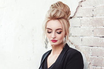 European business woman with evening blond hair style in jacket with earrings on old wall background