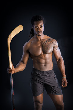 Portrait of a handsome black man posing shirtless for camera with hockey stick in his hands