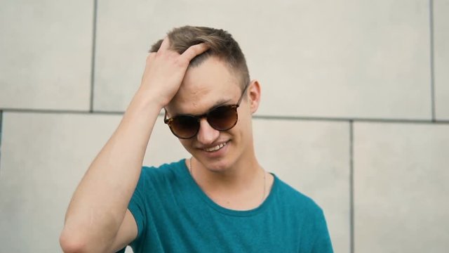 Portrait of young sexy attractive blonde man wears sunglasses before white wall