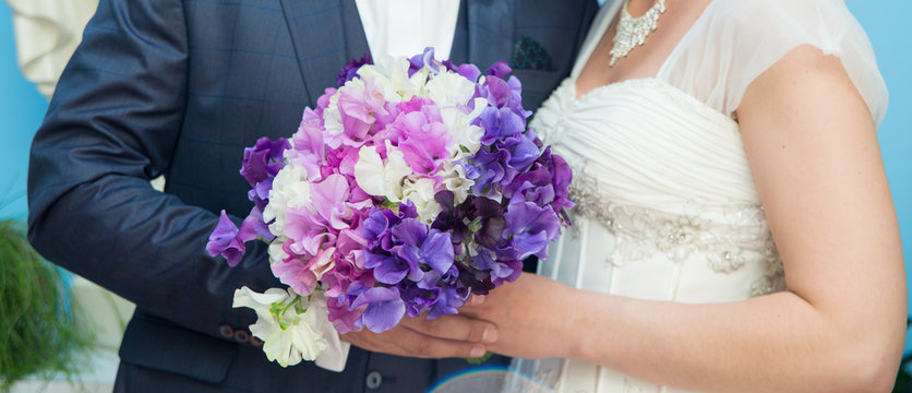 Young just married couple hugging on their wedding day with sweet pea flowers in white wedding dress and dark blue suit
