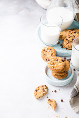 Stack of chocolate chip cookies on blue stone plate with glass of milk on light gray background. Selective focus. Copy space.