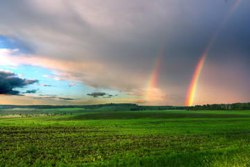 Twin rainbow with overcast sky and green field
