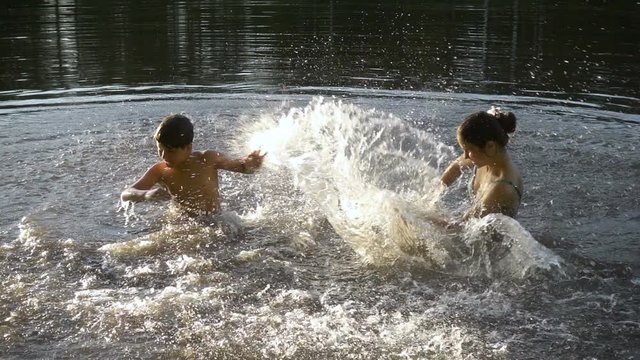 silhouette of two kids splashing water in pond at sunset