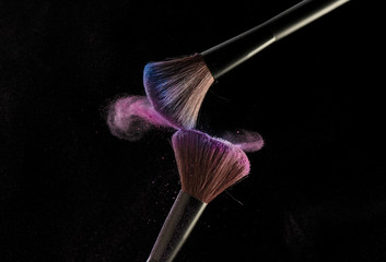 Make-up brushes with pink powder explosion on black background