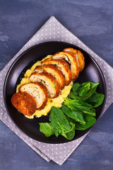 Chicken Kiev on mashed potato with spinach. Breaded chicken breast stuffed with herbs and butter on black plate. View from above, top studio shot
