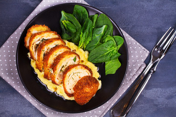 Chicken Kiev on mashed potato with spinach. Breaded chicken breast stuffed with herbs and butter on black plate. View from above, top studio shot