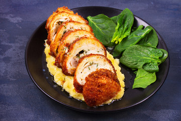 Chicken Kiev on mashed potato with spinach. Breaded chicken breast stuffed with herbs and butter on black plate