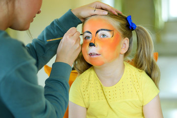 Adorable little girl getting her face painted like tiger by artist