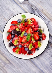 Strawberry, blackberry, blueberry and kiwi salad, garnished with mint. Fruit and berry salad. View from above, top studio shot