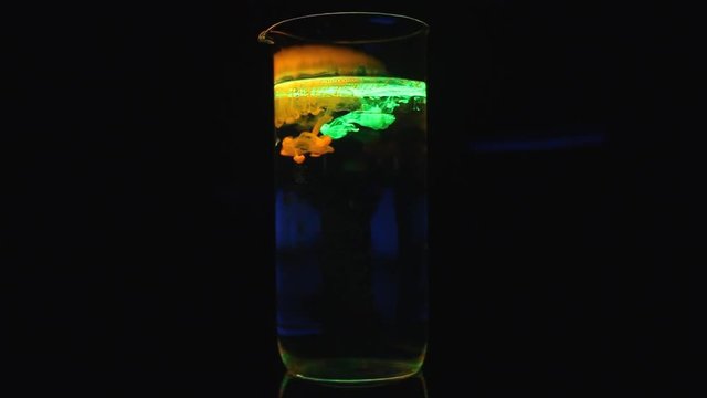 Glowing yellow & green liquid neon ink effect chemicals in shining medical glass under ultraviolet lights.