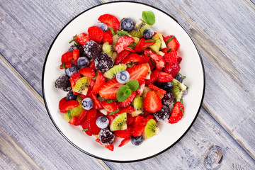 Strawberry, blackberry, blueberry and kiwi salad, garnished with mint. Fruit and berry salad. View from above, top studio shot