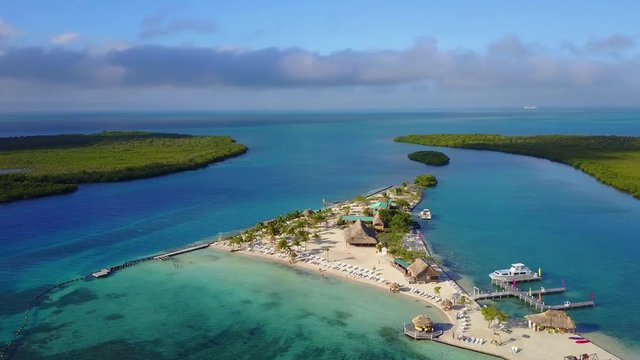 Side view drone shot of island that allows to see amazing crystal blue waters, boats, reefs, and beach life. 