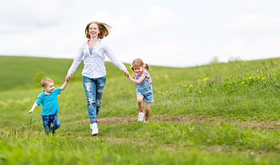 Happy family mother and children daughter and son laughing and running on   meadow in summer