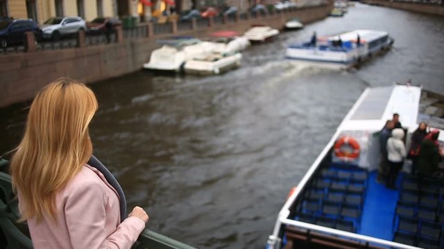 A woman in a coat stands on a bridge and looks down at the black water. She wants to commit suicide