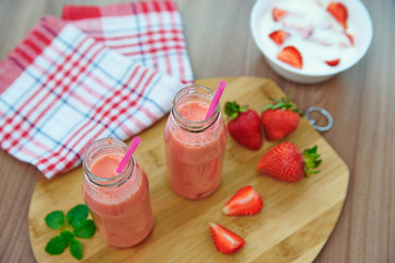 Strawberry smoothies and pieces of strawberries on a wooden board, top view