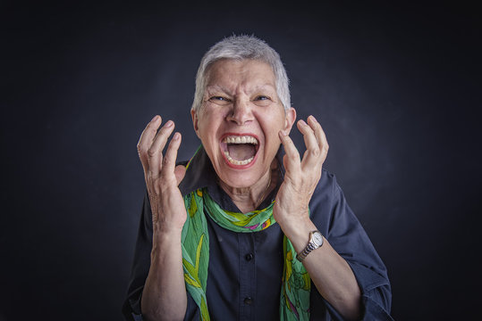 Senior angry enraged woman yelling, pissed off, black background