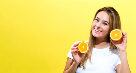 Happy young woman holding oranges halves on a yellow background