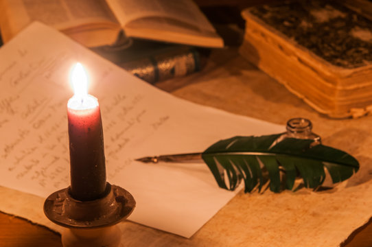 Closeup view of a candle with a quill pen and inkwell in the background