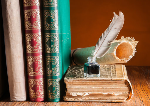 Quill pen and a rolled papyrus sheet on a wooden table with old books