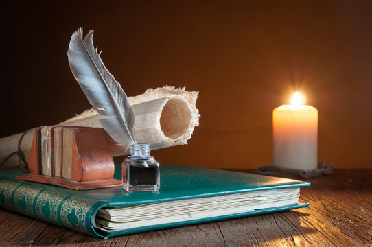 Quill pen and a rolled papyrus sheet on an old book by candle light