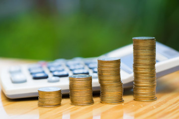 Growing coins and calculator on wood with green tree bokeh background.