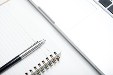 Laptop computer with notebook and pen on white table