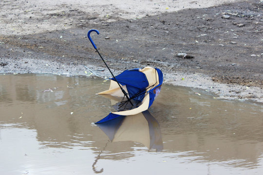 Broken child's umbrella lies in a puddle.