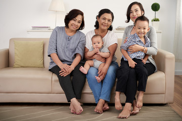 Portrait of  Asian family posing for photo at home, holding two children and  all smiling happily looking at camera in living room