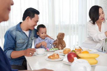 Portrait of Asian man playing with son at breakfast table with family