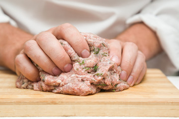 Chef's hands mixing minced meat on the wooden board in the kitchen. Preparation for cooking. Healthy eating and lifestyle.