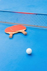 pingpong rackets and ball and net on a blue pingpong table
