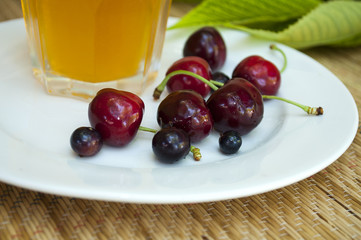 ripe cherry on a white plate with glass of juice