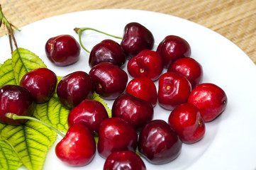 ripe cherry on a white plate with green leaves