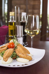 Fried chicken breast on wooden table. Breaded crispy fried chicken tasty dinner. Beautifully served meal at the restaurant. Wine bottles and glass in the background.