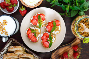 Mini sandwiches with cottage cheese, fresh strawberries, decorated with mint leaves on rye bread on a dark wooden background. Top view. Proper nutrition. Healthy food. Dietary menu.