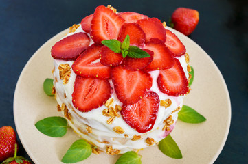 A festive cake with fresh strawberries, cream, decorated with mint leaves on a black background. Top view. Close-up.