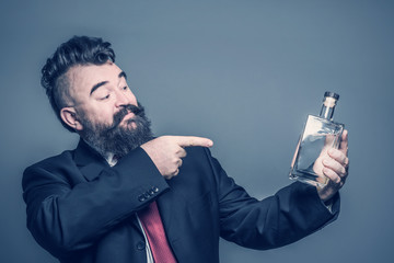 Adult bearded man in suit pointing at a bottle of alcohol in hand
