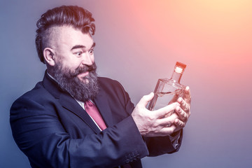 Happy adult bearded man in suit looking at a bottle of alcohol in the sunlight