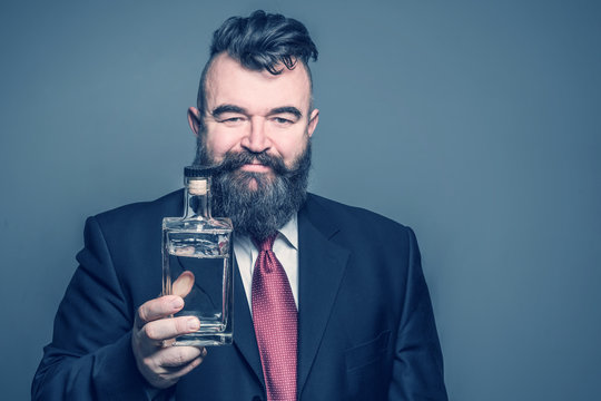 Adult bearded man in suit holding a bottle of alcohol