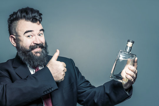 Smiling adult bearded man in suit holding a bottle of alcohol and showing the thumb up