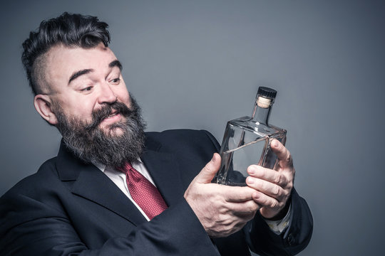 Adult bearded man in suit looking at a bottle of alcohol in his hand