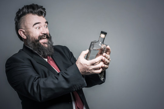Happy adult bearded man in suit looking at a bottle of alcohol in his hand
