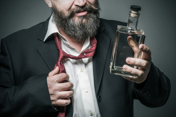 Bearded man in suit holding a bottle of alcohol in his hand