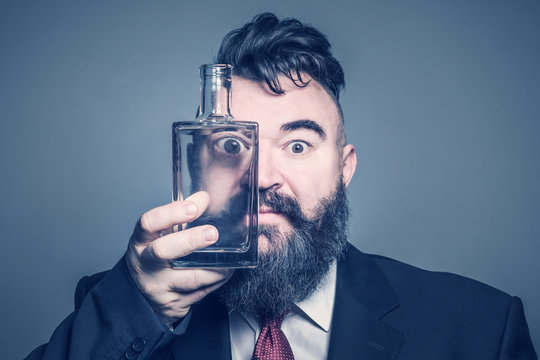 Adult bearded man in suit  looking through a glass bottle of alcohol. Toned