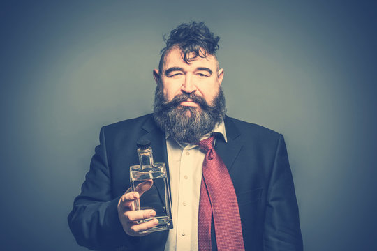 Disheveled adult bearded man in suit holding in his hand a bottle of alcohol. Toned