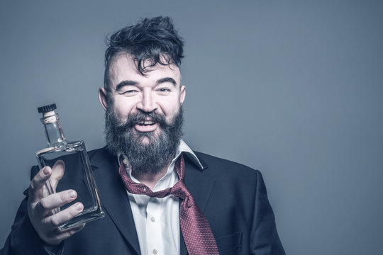 Smiling disheveled bearded man in suit with a bottle of alcohol in his hand. Toned